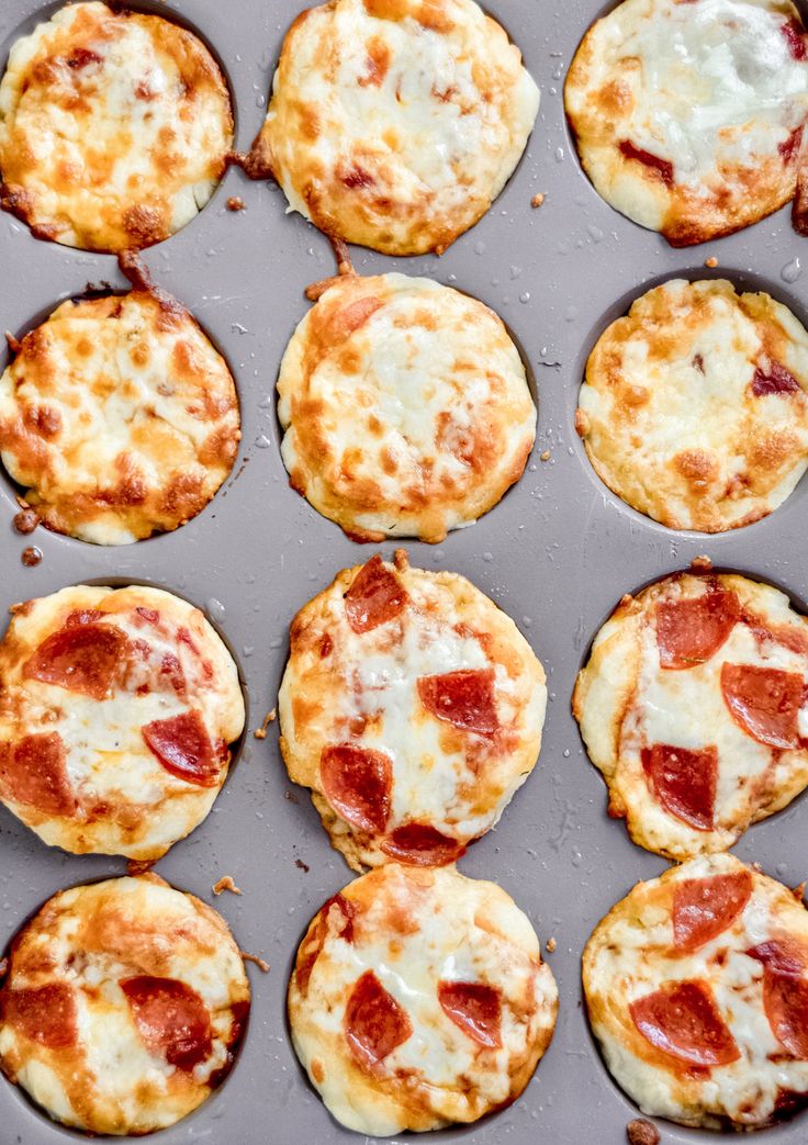 several mini pizzas with cheese and pepperoni are in a muffin tin, ready to be eaten