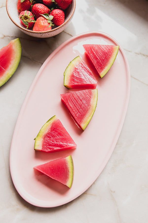 slices of watermelon and strawberries on a pink plate next to a bowl of strawberries