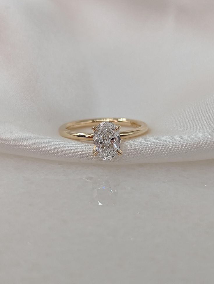 a gold ring with a single diamond on it sitting on a white satin material background