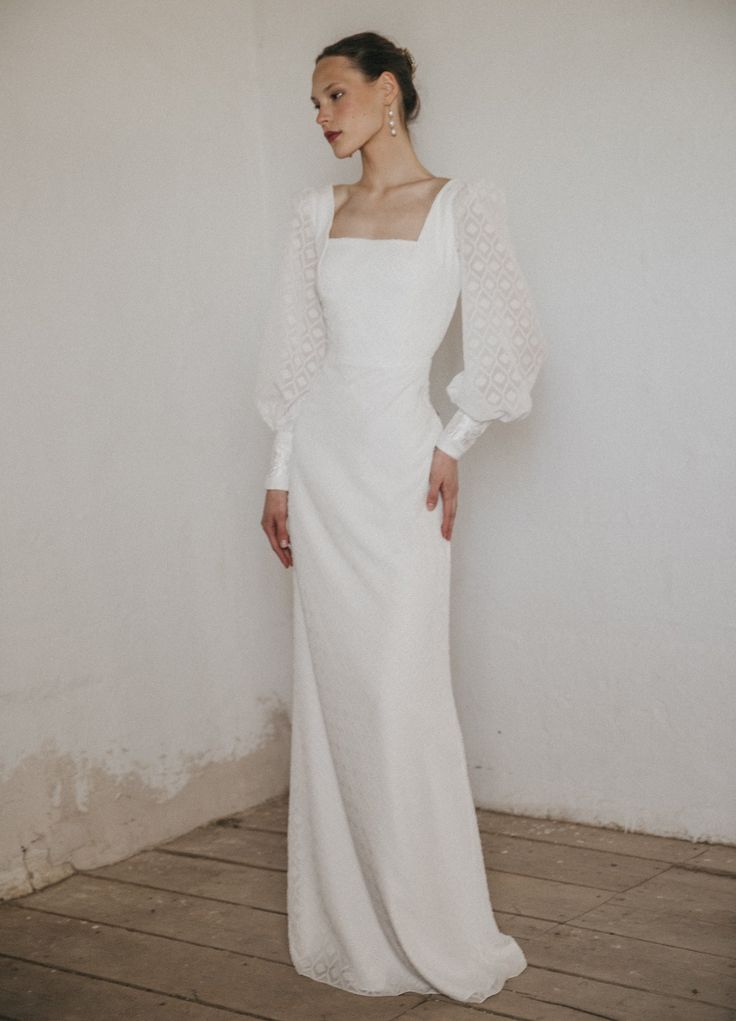 a woman wearing a white dress standing in front of a wall with her hands on her hips