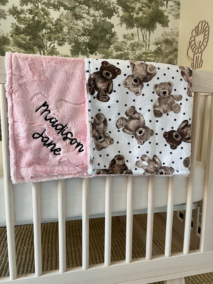 a baby crib with two teddy bears on it and a pink blanket hanging from the rail