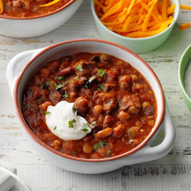 two bowls filled with chili and carrots on top of a white table next to other bowls