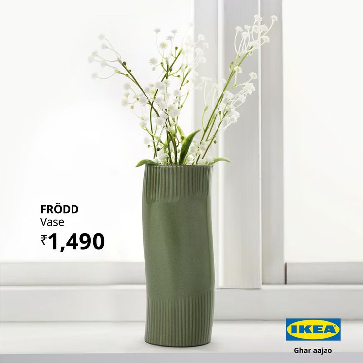 a green vase with white flowers in it sitting on a window sill next to a window