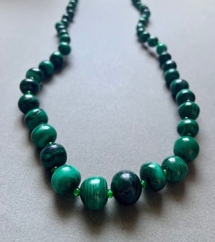 This beaded necklace features large natural malachite beads and small glass beads. Healing Green Onyx Beaded Necklaces, Healing Green Onyx Beaded Necklace, Faceted Green Onyx Round Beaded Necklaces, Green Malachite Beaded Necklaces With Natural Stones, Green Malachite Beaded Necklace With Natural Stones, Turquoise Malachite Necklaces With Round Beads, Green Faceted Beads Spiritual Beaded Necklace, Adjustable Beaded Malachite Necklace, Green Malachite Gemstone Bead Necklaces