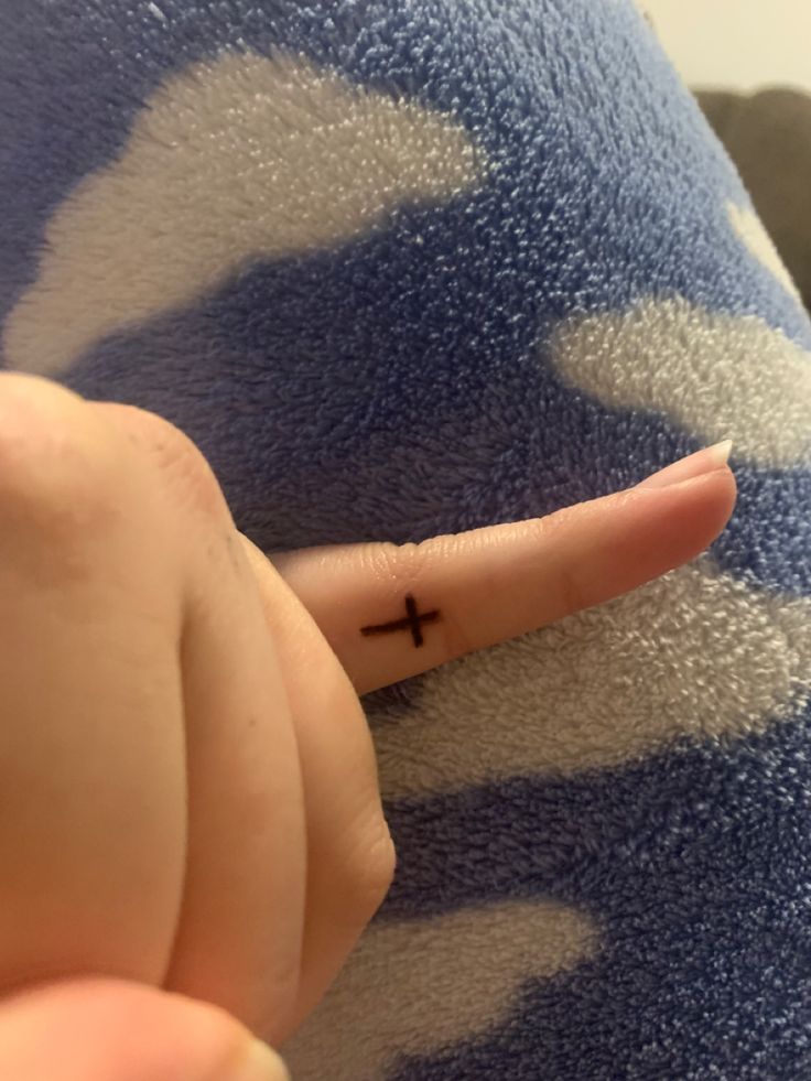 a person's finger with a cross tattoo on it, pointing to the left