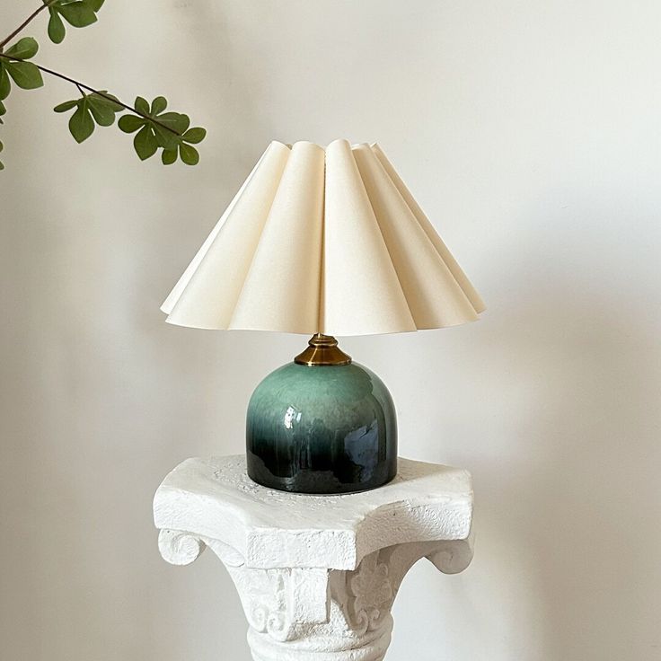 a green lamp sitting on top of a white table next to a plant with leaves