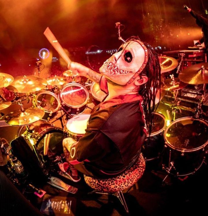 a man with dreadlocks on his face playing drums in front of a crowd