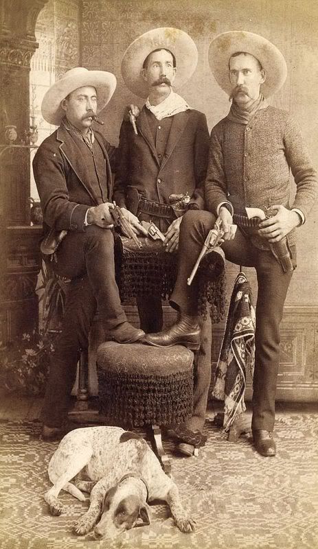 three men in hats are sitting next to a dog