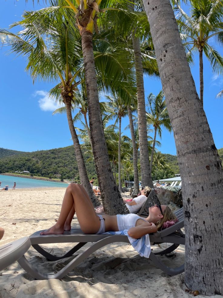 a woman laying on top of a beach next to palm trees