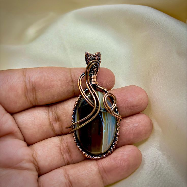 Wire wrapped pendant enthusiasts will adore this beautiful copper wire wrapped pendant, a stunning piece of handmade copper jewelry. This exquisite wire wrapped necklace showcases the artistry and craftsmanship of an artisan jewelry maker. The copper pendant necklace is perfect for those who appreciate unique designs and the intricate beauty of wire wrapped jewelry. With its boho pendant style, this piece adds a touch of bohemian charm to any outfit. Crafted from high-quality copper wire, this j Wire Wrapped Round Pendant Jewelry As Gift, Wire Wrapped Pendant Jewelry Gift, Wire Wrapped Pendant Jewelry For Gifts, Hand Wrapped Round Pendant Jewelry As Gift, Wire Wrapped Agate Pendant Jewelry, Teardrop Agate Wire Wrapped Jewelry, Wire Wrapped Teardrop Agate Jewelry, Agate Round Pendant Jewelry Gift, Agate Round Pendant Jewelry For Gift