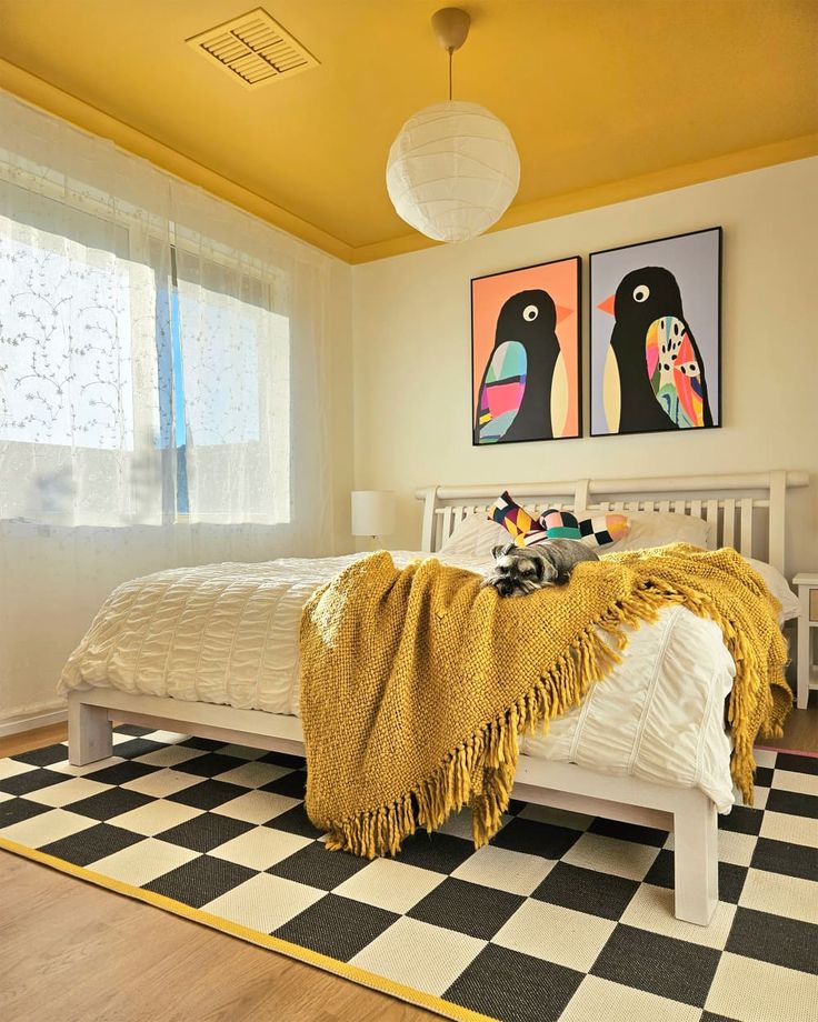 a bedroom with yellow walls and black and white checkered flooring, two paintings on the wall