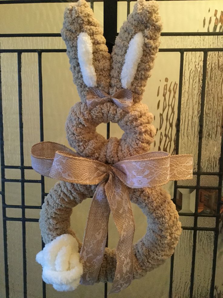 a knitted bunny wreath hanging on a door with a ribbon around it's neck