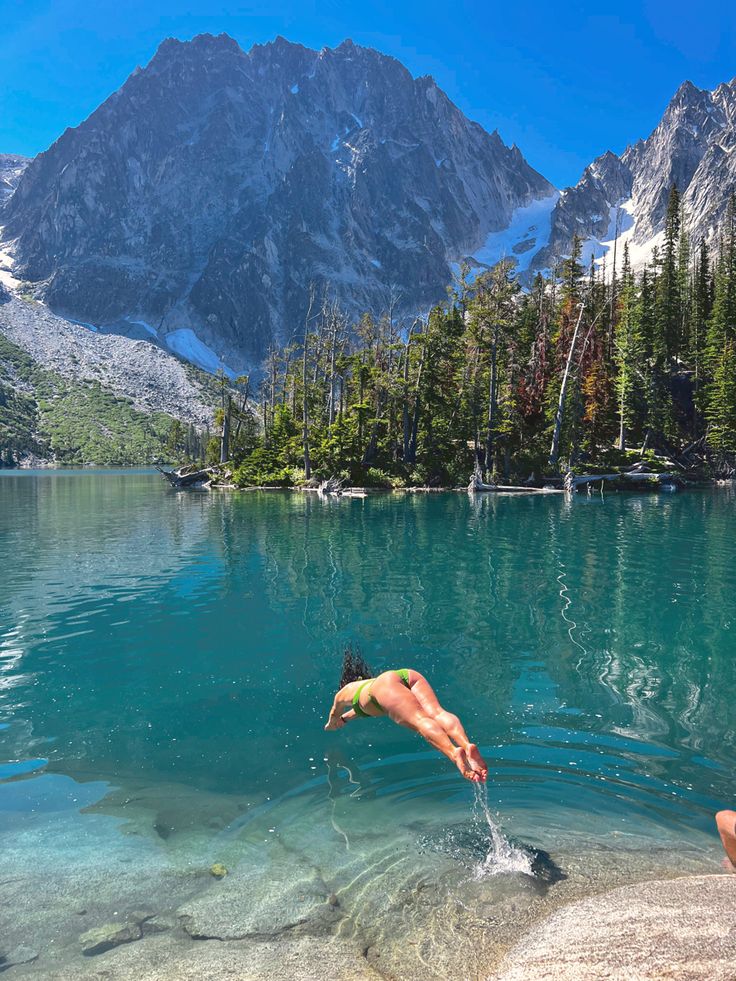 a person diving into a lake with mountains in the background and trees on both sides