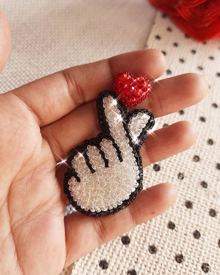 a hand is holding a small brooch with sequins and a red heart