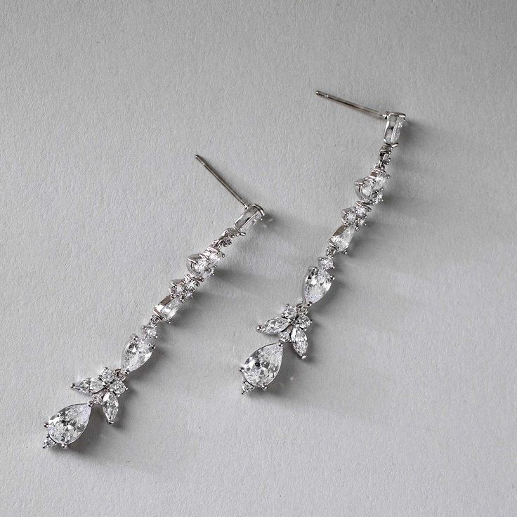 two pairs of diamond drop earrings on a white surface with one earring dangling from the side