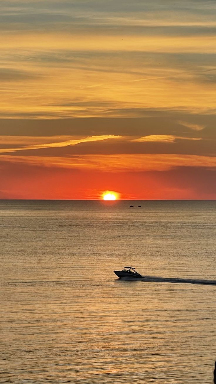 the sun is setting over the ocean with a boat in the water and people walking on the beach