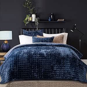 a bed with blue comforter and pillows in a black walled room next to a night stand