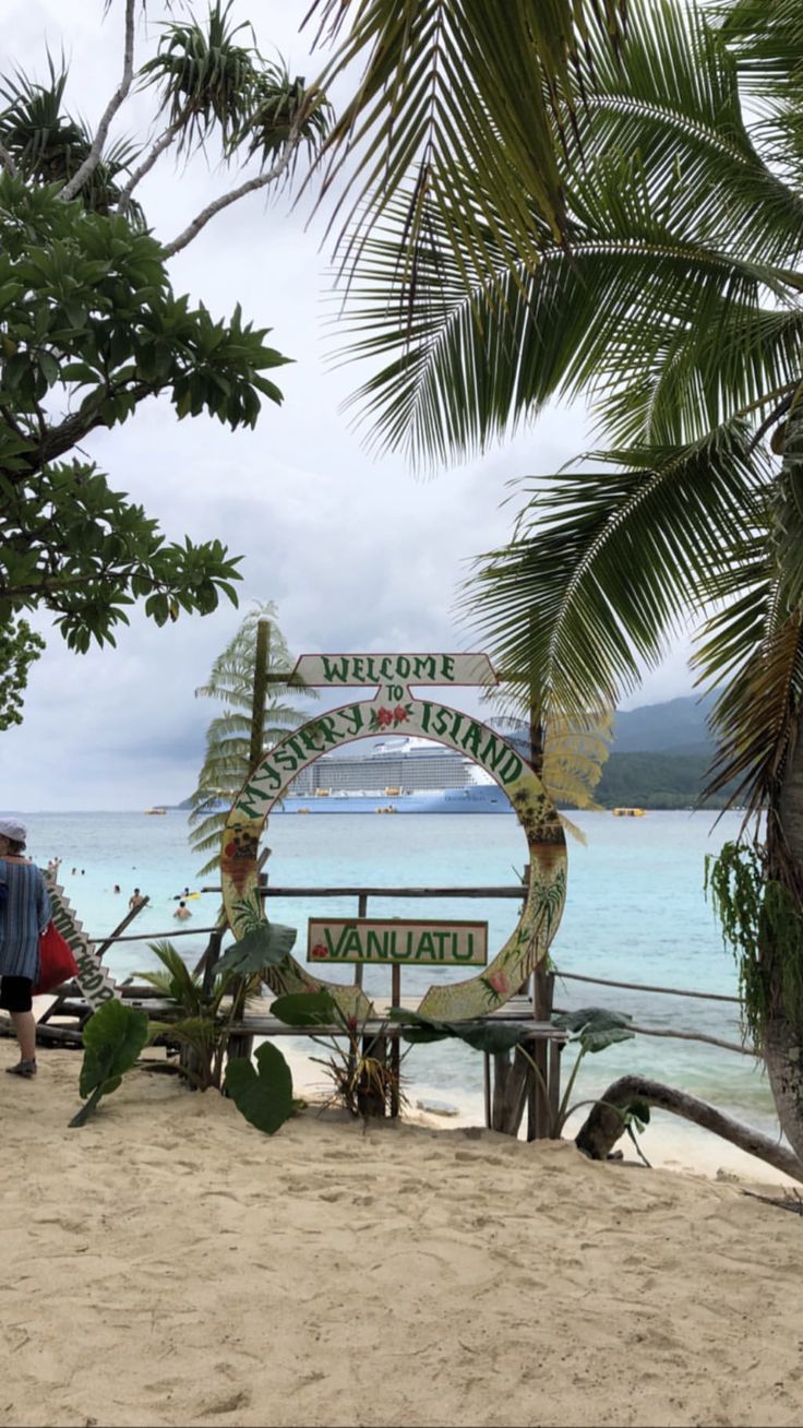 a sign that is on the side of a beach next to some water and palm trees