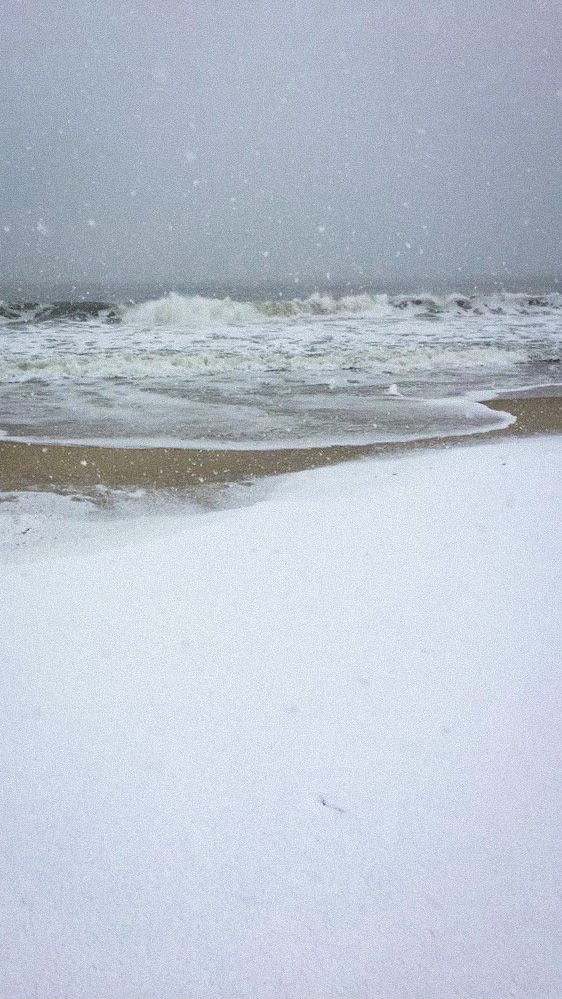 a snowboarder is standing on the beach in front of the ocean and waves