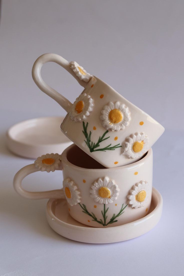 three cups and saucers with daisies painted on them sitting in front of each other