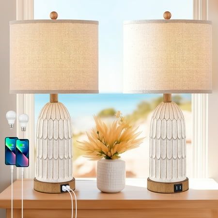 two white lamps sitting on top of a table next to a window with a phone