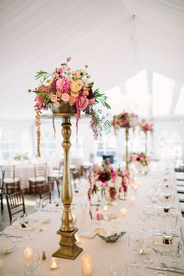 an elegant centerpiece with pink flowers and greenery sits on a long table in a tent