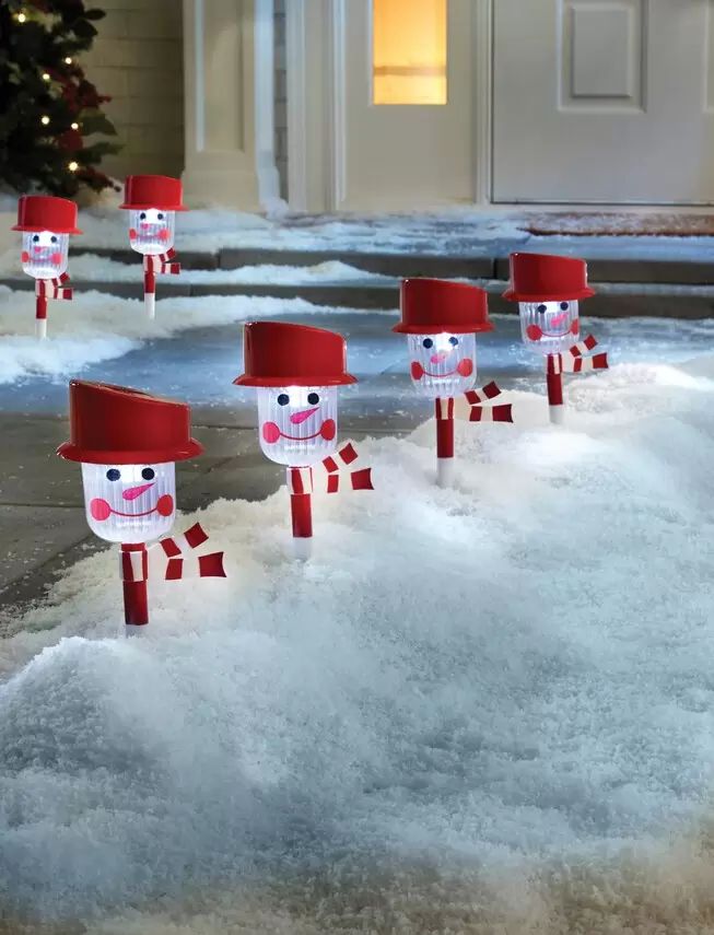 snowmen with red hats and scarfs are in front of a house decorated for christmas