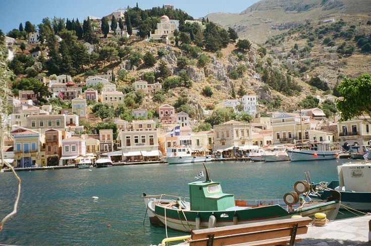 boats are docked in the water next to a hill with houses on it and hills behind them