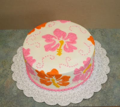 a decorated cake sitting on top of a white doily covered tablecloth with pink and orange flowers