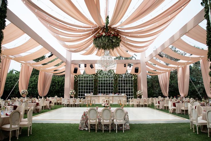 an outdoor wedding venue set up with white linens and pink drapes on the ceiling