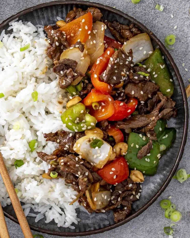 a bowl filled with rice, meat and vegetables next to chopsticks on the side