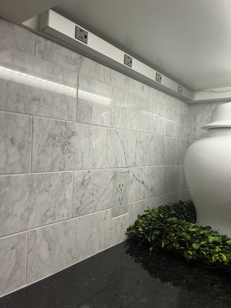 a white vase sitting on top of a black counter next to a wall mounted mirror