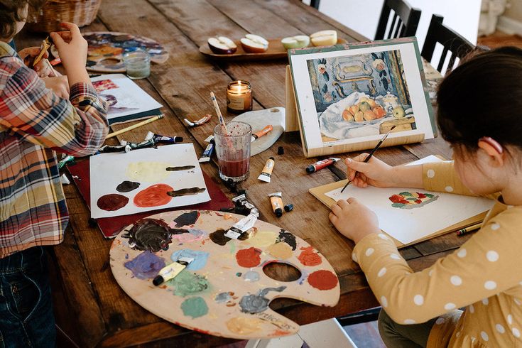 two children sitting at a table with art supplies