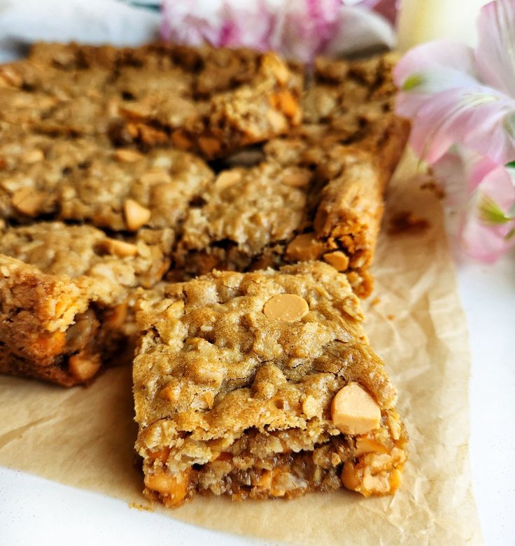 two pieces of granola bar sitting on top of a piece of parchment paper next to flowers