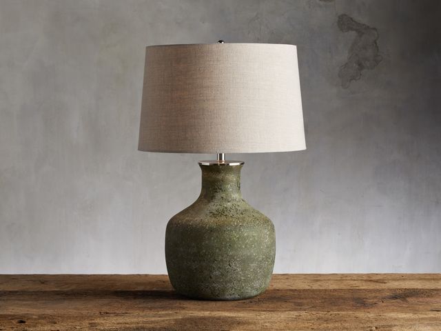 a table lamp sitting on top of a wooden table next to a gray wall with a white shade