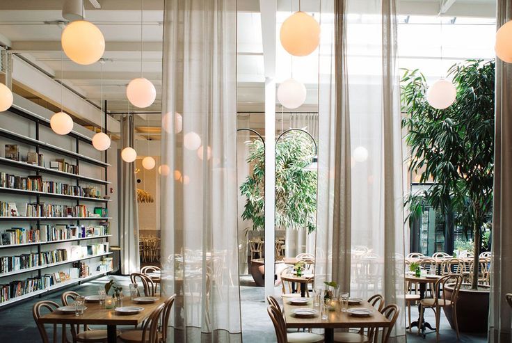 an empty restaurant with tables and chairs in front of large windows filled with bookshelves