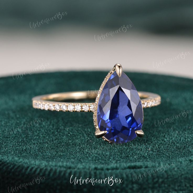 a tan gold engagement ring with a blue sapphire and diamond accents on the band, sitting on a green velvet box