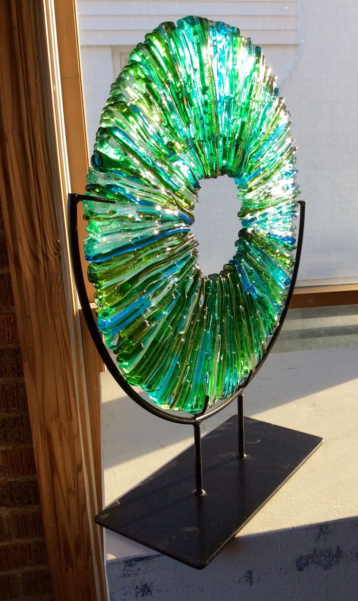 a green glass sculpture sitting on top of a metal stand next to a brick wall