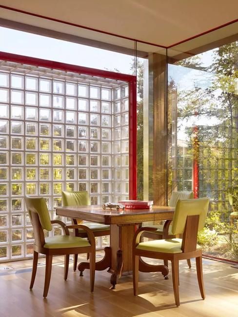 a dining room table with four chairs and a glass block wall in the back ground