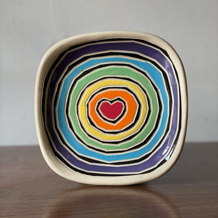 a colorful bowl with a heart painted on the front and sides, sitting on a wooden table