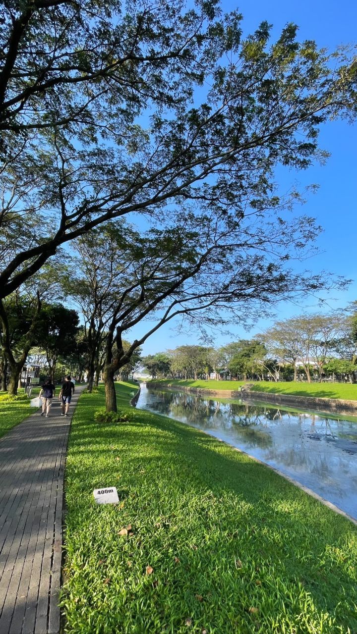 people are walking along the path by the water in the park, near some trees and grass