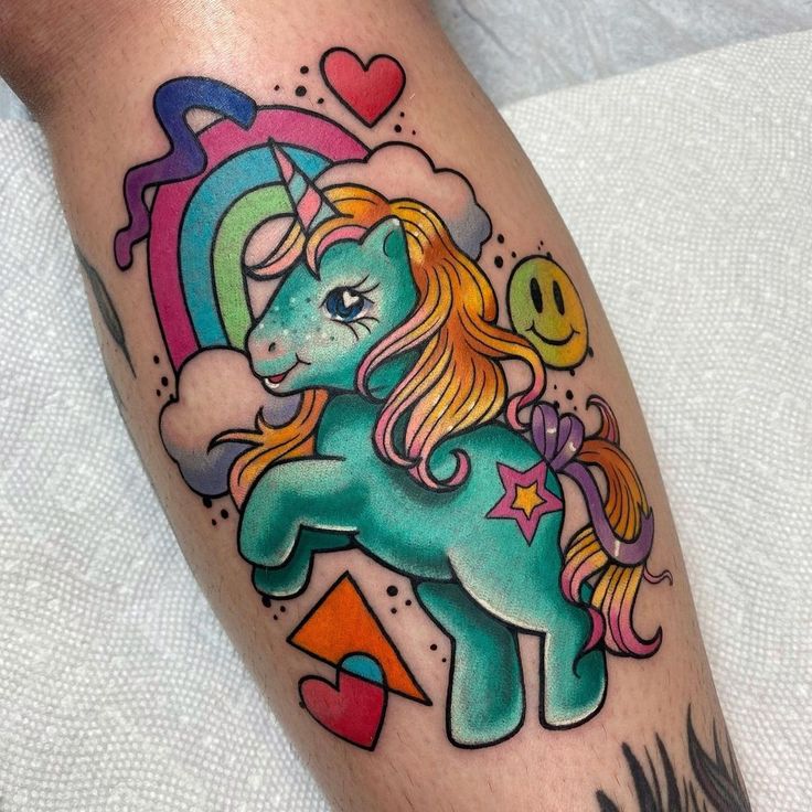 a colorful unicorn tattoo on the leg with rainbows and hearts in the sky behind it