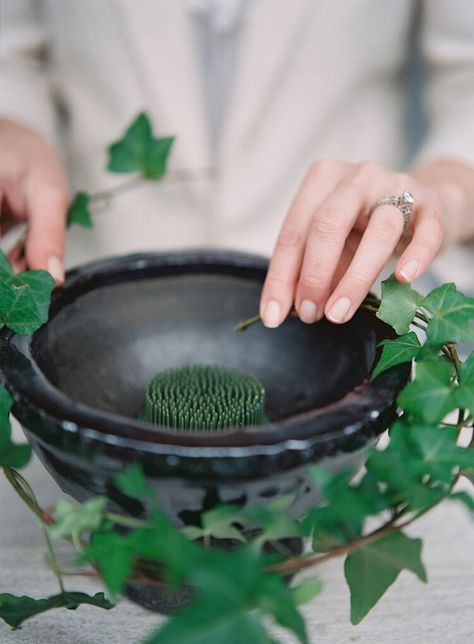 a woman is holding a black bowl with green plants in it and touching the plant