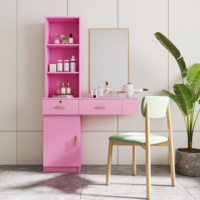 a pink vanity with mirror and stool next to potted plant