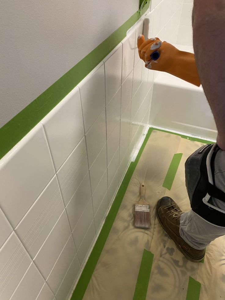 a man is painting the walls in his bathroom with green and white stripes on the floor