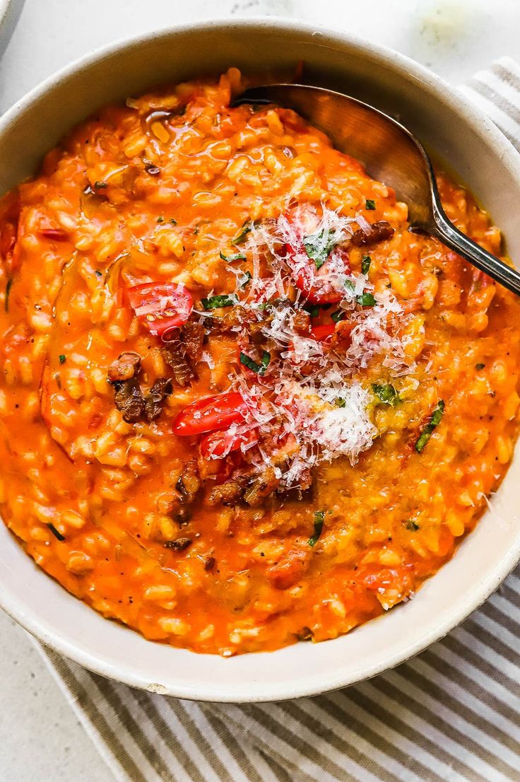 a white bowl filled with pasta and topped with parmesan cheese, tomatoes and herbs