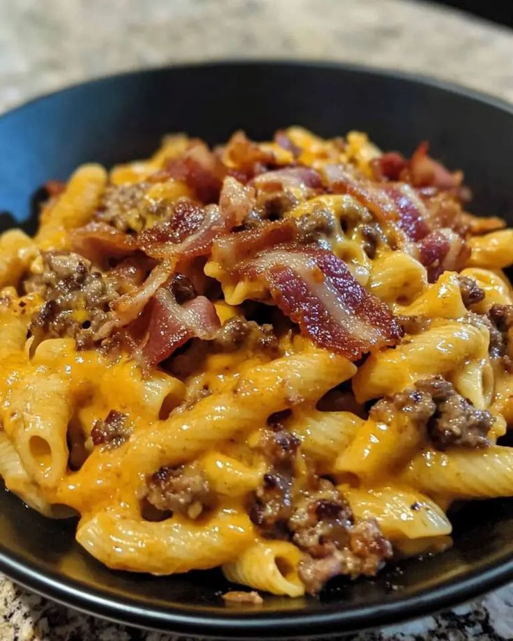 a black bowl filled with macaroni and cheese covered in bacon