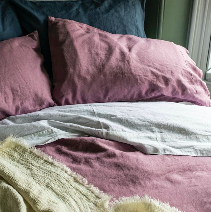 an unmade bed with two pillows and blankets on it's sides, in front of a window