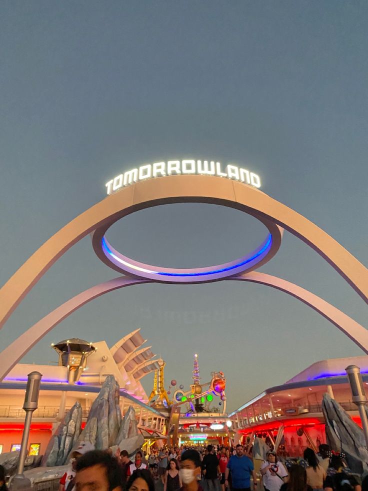 the entrance to tomorrowland at night with people walking under it and onlookers