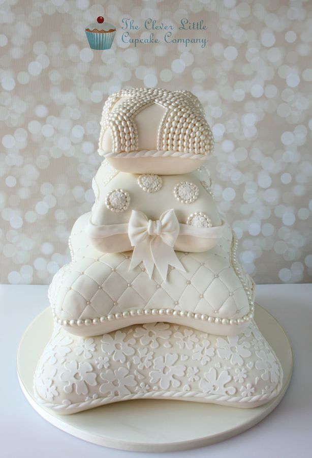 a three tiered white cake with pearls and bows on it's top, sitting on a plate